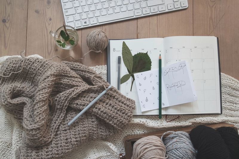 Labor de crochet a medio hacer con la aguja puesta, junto a una libreta con anotaciones y ovillos de hilo
